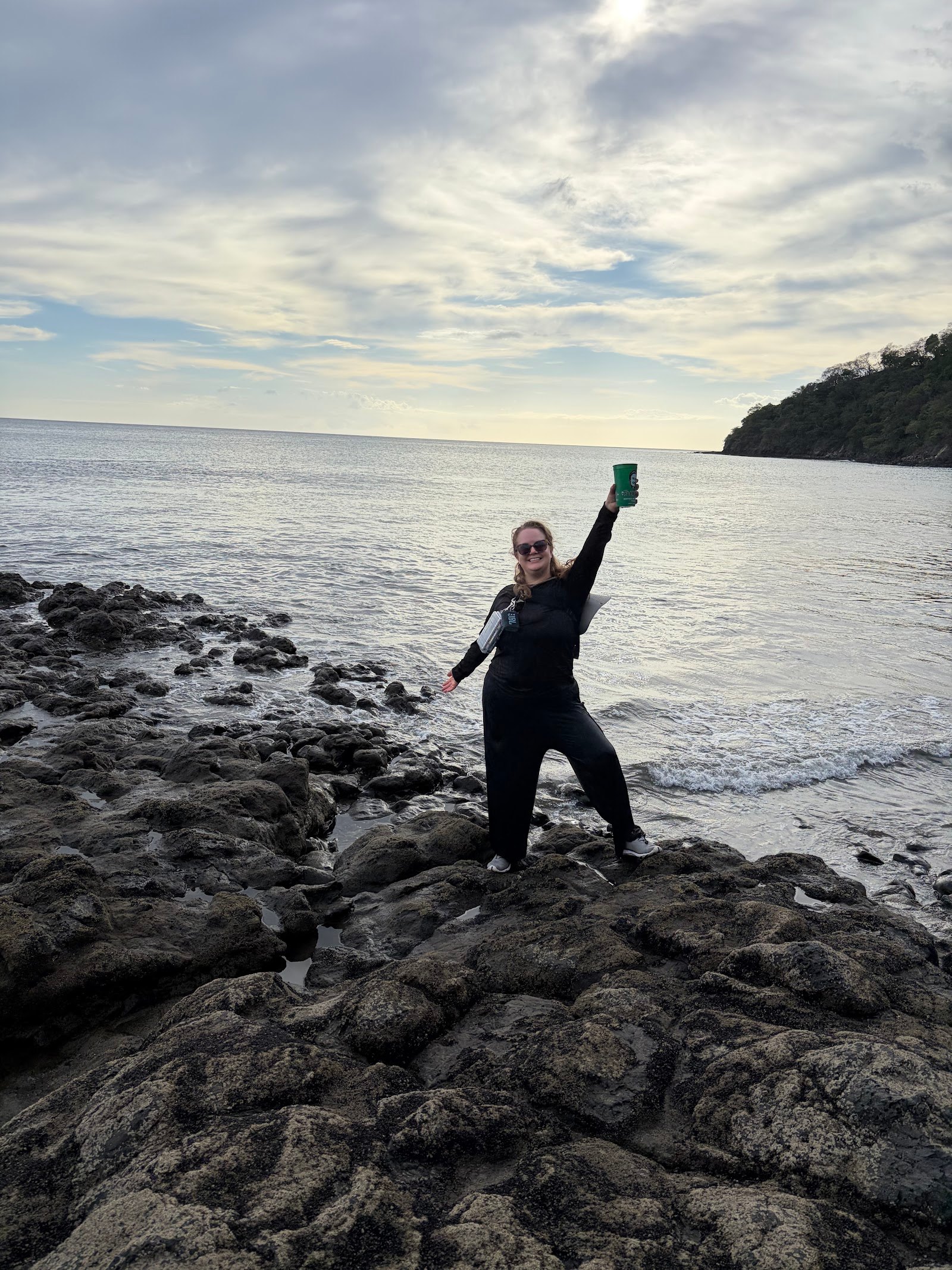 Travel advisor Mari Bay standing on the rocks at the edge of the bay in Playas del Coco, Costa Rica, raising a green cup